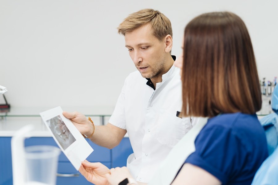 Odontólogo explicando a paciente los efectos de la pérdida de hueso alveolar observados en una radiografía dental.