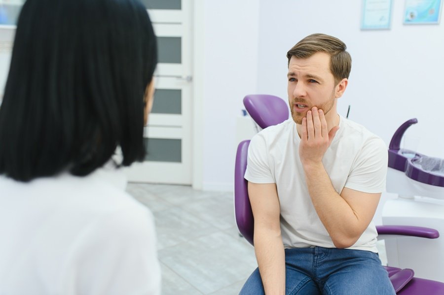 Hombre joven en gabinete dental con dolor en la cara. Síntomas visibles de dolor facial durante una consulta odontológica, asociados al impacto del estrés y salud dental.