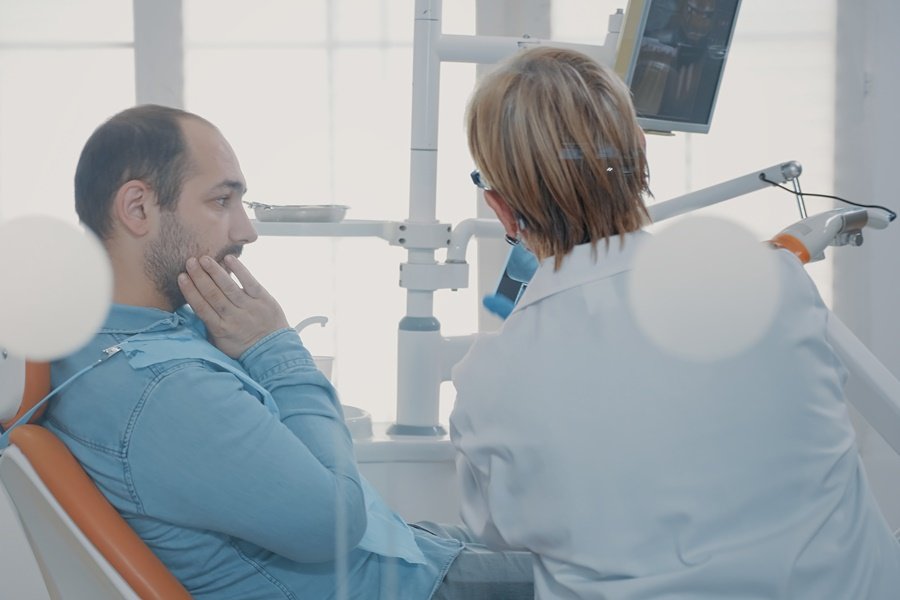 Paciente masculino de alrededor de 50 años, con expresión preocupada durante la consulta con su odontólogo sobre molestias en la mandíbula, posibles efectos del estrés y salud dental.
