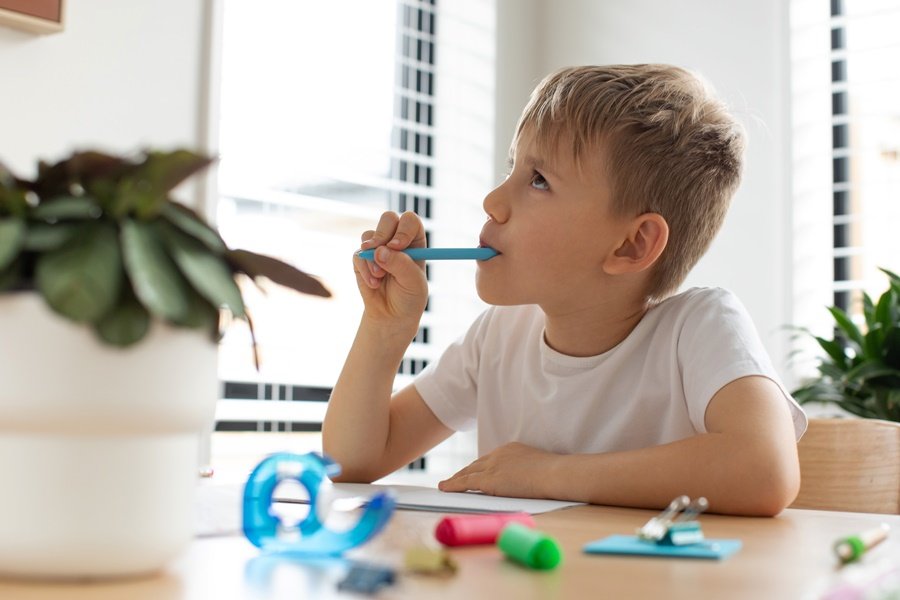 Niño mordiendo un bolígrafo mientras estudia, un mal hábito oral común que puede afectar el desarrollo dental.