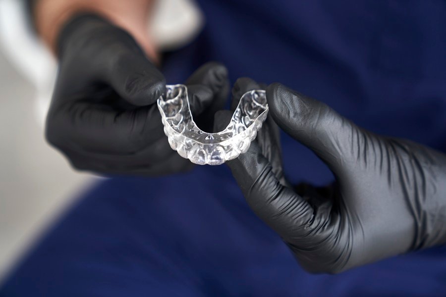Primer plano de un profesional con guantes negros sosteniendo un retenedor post-ortodoncia transparente, utilizado para mantener los resultados de la ortodoncia.