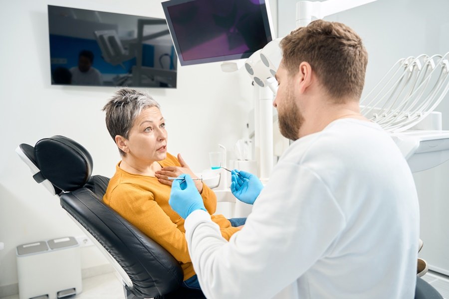Paciente adulta explicando síntomas al dentista durante una consulta, en una posible evaluación por síndrome de la boca ardiente.