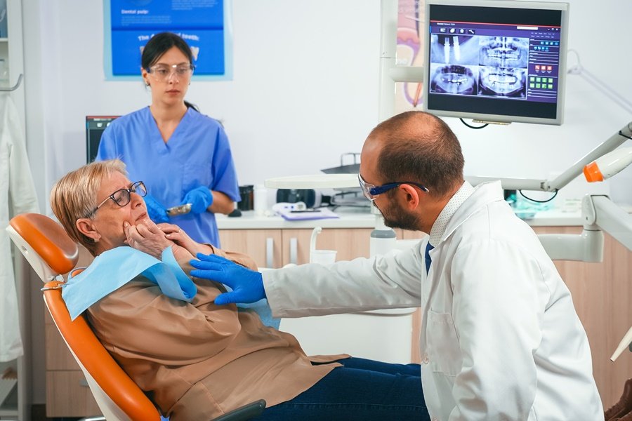 Paciente mayor consultando con su dentista sobre problemas asociados al envejecimiento dental, mientras observa una radiografía bucal en la clínica junto al profesional.
