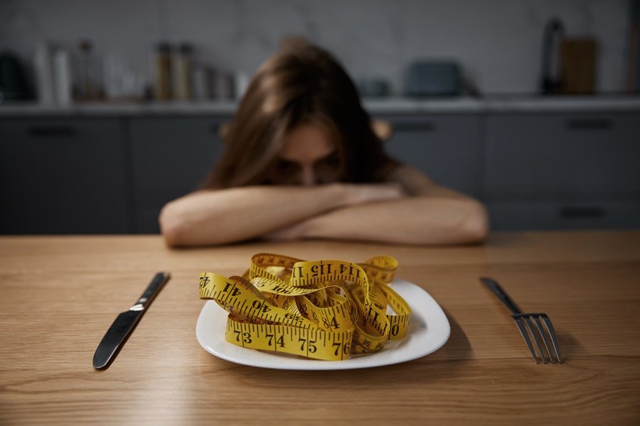 Imagen conceptual sobre trastornos alimentarios y salud dental con una joven frente a un plato con cinta métrica.
