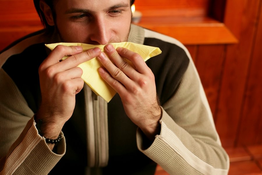 Hombre joven usando una servilleta para secar el exceso de saliva, una manifestación habitual de hipersalivación.