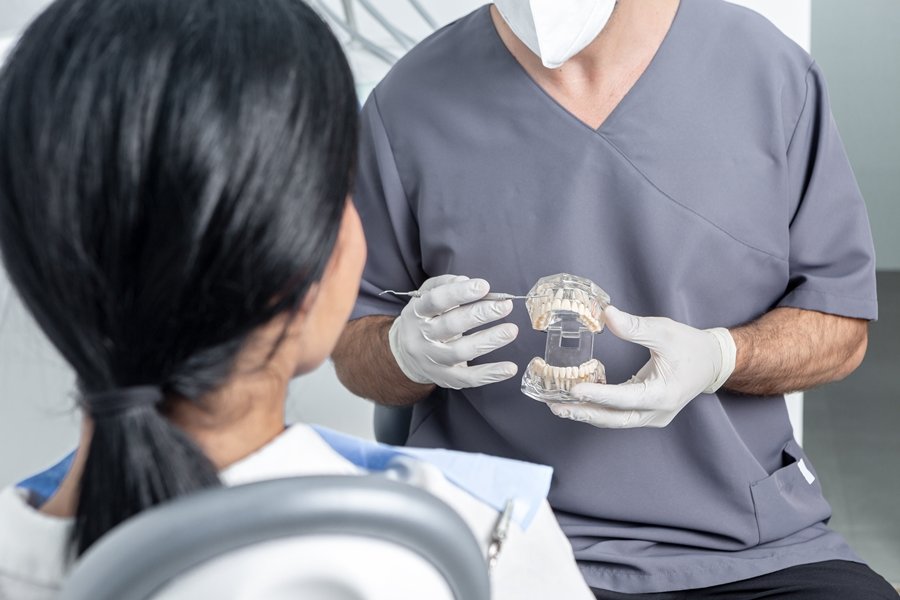 Dentista con guantes mostrando a una paciente un modelo de mandíbula para ilustrar qué es un implante cigomático y cómo ayuda a rehabilitar el maxilar superior.