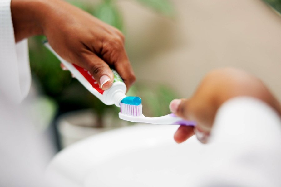 Mano aplicando pasta dental azul sobre un cepillo de dientes, preparando una rutina de limpieza oral con un dentífrico adecuado a las necesidades diarias.