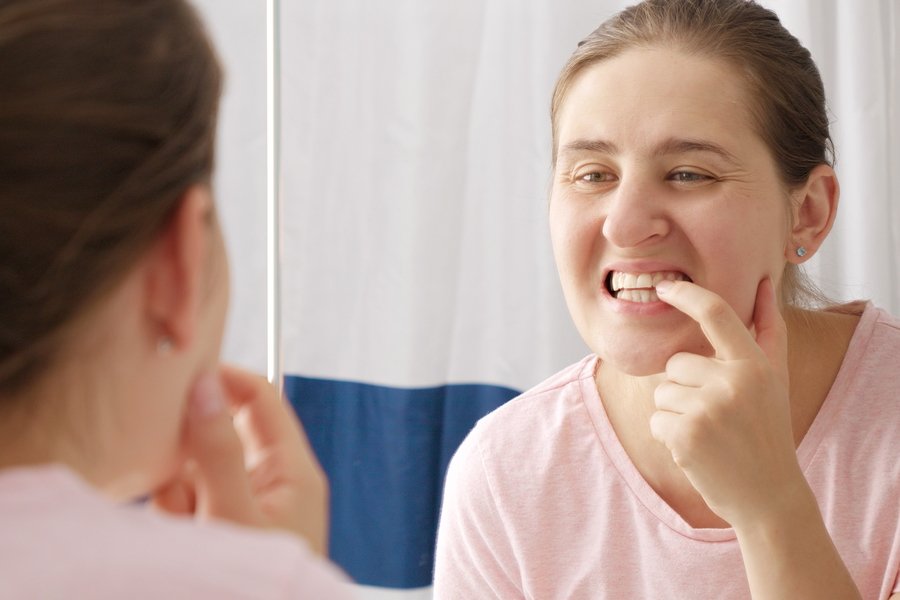 Mujer observando sus encías frente al espejo y señalando una zona con retracción gingival, signo visible del desplazamiento del tejido gingival.