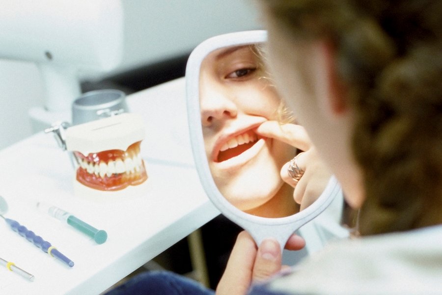 Paciente revisando en un espejo de mano una posible retracción gingival durante una consulta odontológica, con instrumental dental sobre la mesa.