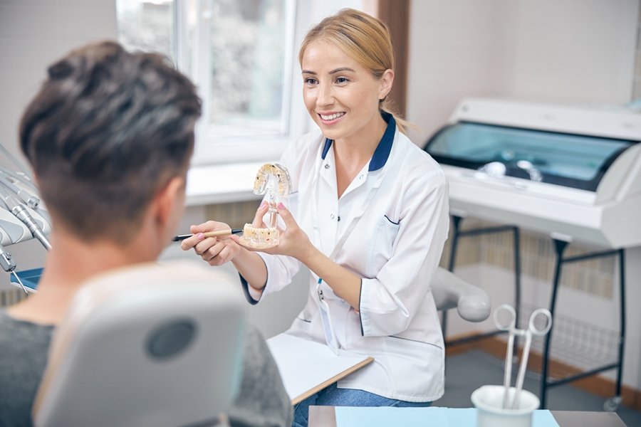 Odontóloga explicando a un paciente la relación entre vitamina D y salud dental con un modelo de mandíbula durante una consulta profesional.