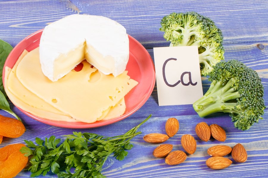Alimentos ricos en calcio como queso, brócoli, almendras y vegetales, acompañados del símbolo químico del calcio, en una composición visual que destaca la relación entre calcio y salud dental.