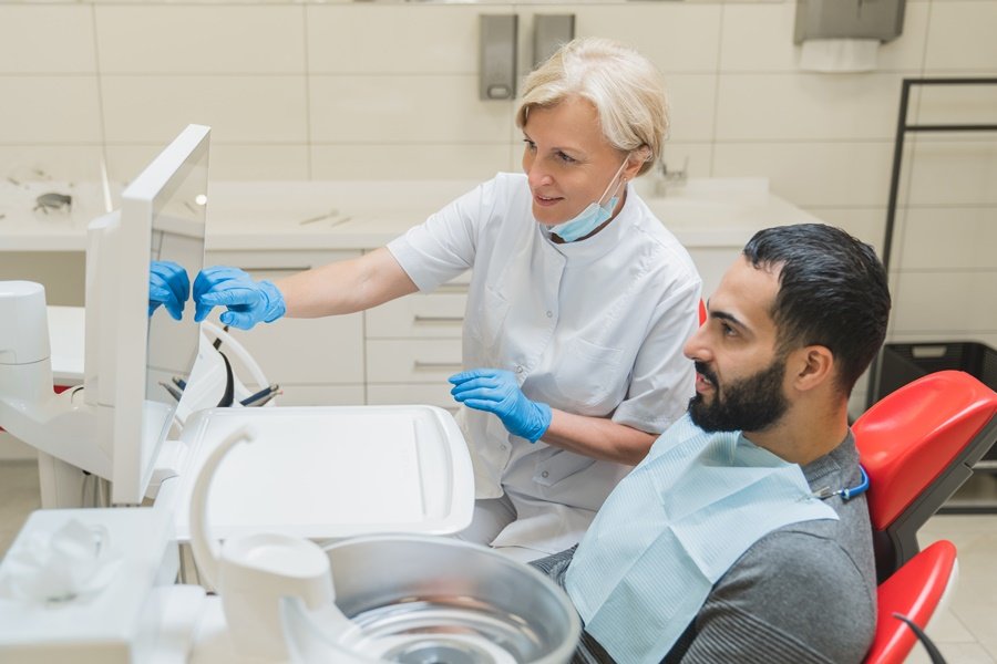 Dentista mostrando en el monitor los resultados del diagnóstico a un paciente con dientes de leche en adultos, en clínica equipada con tecnología avanzada.
