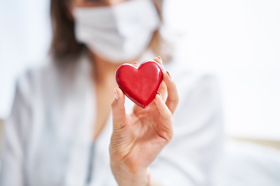 Profesional de la odontología con mascarilla sostiene una figura de corazón rojo, simbolizando la conexión entre enfermedades cardiovasculares y salud bucodental.